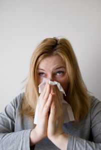 Picture of a woman blowing her nose to indicate that she is sick, to illustrate that good judgement is needed to decide if you should practice qigong when sick