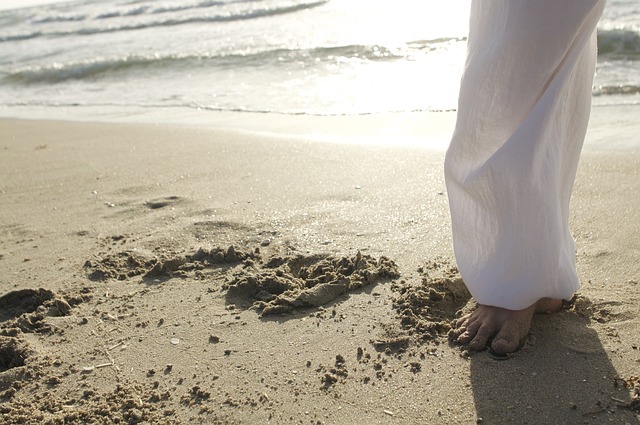 A foot standing on sand with a wave in the background, showing the connection to earth and water while practicing qigong