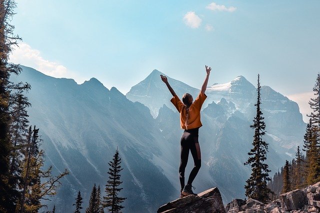 Woman on mountain with arms raised, showing her taking pleasure in her success